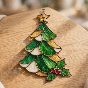 May include: A stained glass Christmas tree ornament featuring layered green, gold, and white glass segments. The tree is topped with a gold star and decorated at the base with green holly leaves and two small, round, red glass berries.