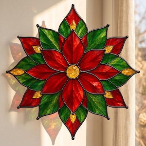 May include: A stained glass poinsettia suncatcher featuring a symmetrical star-shaped design with vibrant red, deep green, and golden yellow textured glass panels held together by dark metal lead lines, casting colorful light reflections.