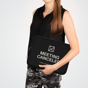 Könnte beinhalten: Eine schwarze Laptoptasche mit einer weißen Grafik eines Kalenders mit einem X-Symbol und dem Text "MEETING CANCELED" gefolgt von "> STATUS: ESCAPED". Die Tasche ist rechteckig mit abgerundeten Ecken und einem seitlichen Reißverschluss.