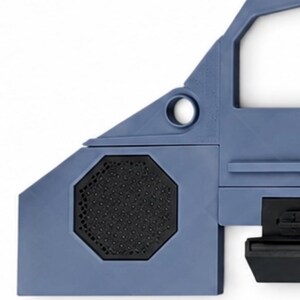 May include: A blue plastic component featuring an angular frame with a circular opening and a black octagonal speaker grille insert. The structure includes a flat horizontal edge and a black mechanical attachment piece extending from the side.