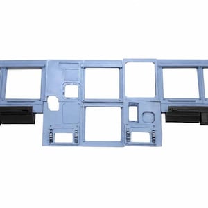 May include: A light blue aircraft cockpit instrument panel frame featuring multiple rectangular cutouts for gauges and displays, with black horizontal ledges and circular speaker grilles positioned on the far left and right sides of the structure.