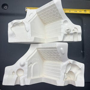 May include: Two white ceramic slip casting molds for a dog house, featuring embossed roof shingles and wood grain textures. The molds include the text "PLUTO" and "WALT DISNEY PROD". A yellow measuring tape shows the width is over 12 inches.