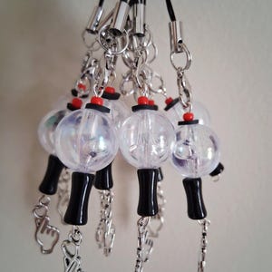 May include: A collection of phone charms featuring clear, iridescent spherical beads atop black cylindrical bases, accented with small red rings. Each charm includes a silver-toned metal lobster clasp and a dangling hand gesture charm.
