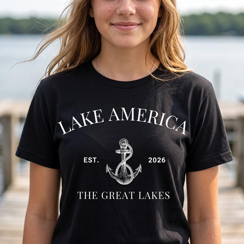 Peut inclure: Un t-shirt noir &agrave; manches courtes avec le texte blanc LAKE AMERICA, EST. 2026 et THE GREAT LAKES. Un graphique blanc d&eacute;taill&eacute; repr&eacute;sentant une ancre marine entour&eacute;e d'une corde est centr&eacute; entre la date de cr&eacute;ation et le texte.