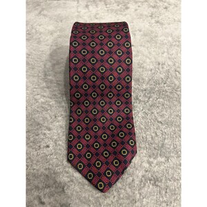 May include: A necktie featuring a dark navy blue background with a repeating geometric pattern of small yellow octagons and elongated red rectangular shapes arranged in a grid-like formation across the entire surface of the fabric.