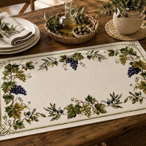 May include: A rectangular placemat featuring a cream-colored center and a decorative border printed with green grape leaves, clusters of purple and green grapes, and small black olives. The design is framed by a thin, dark green line.