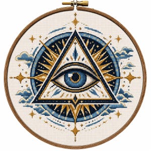 Könnte beinhalten: Ein runder Stickrahmen aus Holz mit einem Kreuzstichmuster, das ein allsehendes Auge in einem Dreieck zeigt. Das Design besteht aus dunkelblauem, hellblauem und goldenem Garn, umgeben von stilisierten Wolken und vierzackigen Sternformen.
