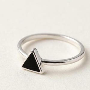 May include: A polished silver ring featuring a single, small, solid black triangle inlay centered on the band. The metal has a smooth, reflective finish, and the triangular accent is set flush within the silver frame of the ring's design.