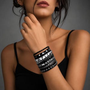 May include: A multi-layered bracelet set featuring black leather bands and metallic silver-toned accents. The design includes rows of pyramid studs, smooth spherical beads, and a braided leather cord, creating a stacked appearance on the wrist.