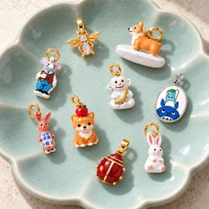 May include: A collection of gold-toned metal charms featuring enamel designs including a bee, a corgi, a mouse in a vest, a monkey with a banana, a rabbit with a blue apron, a corgi with an apple, a ladybug, a white rabbit, and a blue character pendant.