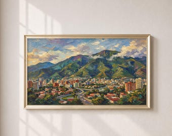 May include: An oil painting in a gold frame depicting a city nestled at the base of a large, green mountain range under a blue sky with white clouds. The landscape features numerous buildings with red roofs, winding roads, and lush vegetation.