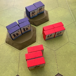 May include: A board game set featuring purple and red wooden blocks with printed soldier illustrations and text labels like LINE and LIGHT. The blocks are arranged in groups on two brown hexagonal bases, with some blocks placed directly on the green board.