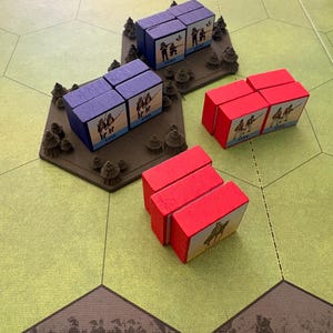 May include: A set of wooden board game blocks featuring purple and red rectangular units. The purple units are mounted on brown hexagonal bases with small tree details. Each block displays printed illustrations of soldiers and the text LINE or LIGHT.