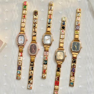 May include: Five gold-tone wristwatches with rectangular faces and link bracelets featuring colorful enamel charms. The watches have various dial colors including white, brown, and black, with some bezels accented by small clear stones.
