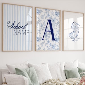 May include: Three framed wall art prints with light wood frames. The left print has blue vertical stripes and the text School NAME. The center print features a blue floral pattern with a large letter A. The right print shows a blue New Jersey map.