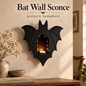 Op de afbeelding: Een zwarte vleermuisvormige wandlamp met een centrale boogvormige uitsparing waarin een klein brandend waxinelichtje staat. De tekst "Bat Wall Sconce pottery template" staat erboven in een donker schreeflettertype met een icoon.