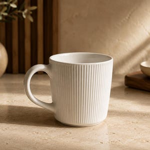 May include: A white ceramic mug featuring a vertical ribbed texture on the exterior surface. The mug has a smooth, curved handle on the left side and a wide, open top rim. The design is consistent throughout the body of the vessel.