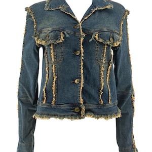 Puede incluir: Una chaqueta de mezclilla azul oscuro con cuello clásico, mangas largas y cierre frontal de botones. La prenda presenta costuras deshilachadas y bordes sin rematar en un color beige contrastante a lo largo del cuello, los bolsillos y el dobladillo.