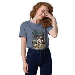 May include: A heather blue short-sleeve t-shirt featuring a graphic of a husky dog looking out of a vehicle window. The text reads Mi COPILOTO tiene pelo Y TIENE 4 PATAS, accompanied by illustrations of mountains, pine trees, and a compass.