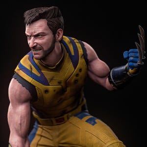 Op de afbeelding: Een gedetailleerd figuur met kort donker haar en een baard, gekleed in een geel en blauw tactisch pak met gestructureerde bepantsering. Het figuur heeft metalen klauwen uitgestoken vanuit blauwe handschoenen en staat in een dynamische houding.