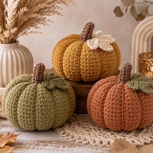 Può includere: Tre zucche all'uncinetto nei colori verde salvia, giallo senape e arancione bruciato. Ogni zucca presenta una superficie testurizzata a coste, un gambo all'uncinetto marrone scuro e una foglia all'uncinetto attaccata alla parte superiore.