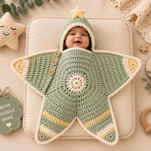 Peut inclure: Une couverture d'emmaillotage pour bébé en crochet vert sauge en forme d'étoile avec une capuche surmontée d'une petite étoile jaune. Elle présente une bordure crème, trois boutons en bois sur le côté et un motif circulaire central.