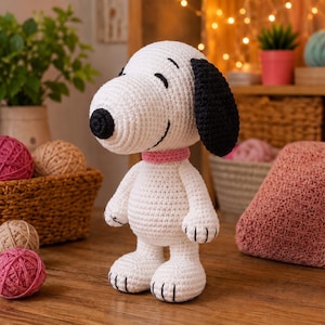 May include: A white crocheted stuffed animal resembling a beagle with a black nose, black ears, and a pink collar. The figure has a rounded head, a small body, and stitched details on the feet. The texture is consistent with yarn craft.
