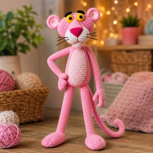 May include: A handmade crochet doll of a tall, slender pink panther character. The figure features a bright pink body with a lighter pink belly patch, yellow eyes with black pupils, black eyebrows, a dark pink nose, and black stitched whiskers.