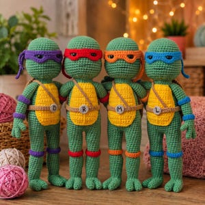 Puede incluir: Cuatro muñecos de tortuga tejidos a ganchillo en color verde, de pie en fila. Cada uno lleva un antifaz de color, muñequeras y tobilleras a juego, y un peto beige. Los antifaces son morados, rojos, naranjas y azules. Cada cinturón tiene una letra D, R, M o L.