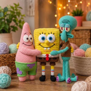 Puede incluir: Tres peluches de ganchillo que representan personajes de dibujos animados: una estrella de mar rosa con pantalones cortos verdes, una esponja rectangular amarilla con camisa blanca y pantalones marrones, y una figura turquesa con camisa marrón.