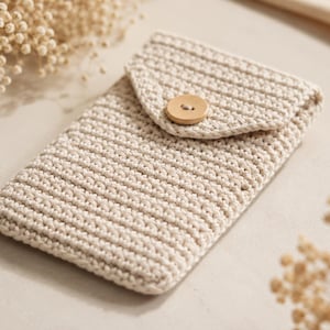 May include: A rectangular beige crochet pouch featuring a textured stitch pattern and a triangular flap closure secured with a single round wooden button. The pouch is constructed from thick yarn and maintains a consistent neutral color throughout.