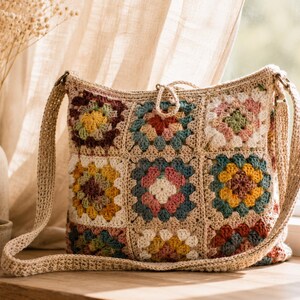 May include: A crochet shoulder bag featuring a grid of nine square motifs in various colors including yellow, blue, pink, and dark red, all bordered by a neutral beige yarn. The bag has a matching beige crochet strap and a small loop closure at the top.