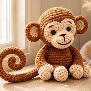 Könnte beinhalten: Ein gehäkeltes Affen-Stofftier in Braun und Beige mit einem langen, geringelten Schwanz. Der Affe hat einen runden Kopf, große Ohren, dunkle Kunststoffaugen und einen gestickten Mund. Der Körper besteht aus strukturiertem Garn mit hellen Pfoten.
