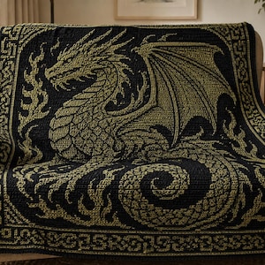 May include: A rectangular crochet blanket featuring a black and gold color scheme. The design displays a large, detailed dragon in the center, surrounded by stylized flames and a geometric border pattern that frames the entire piece.