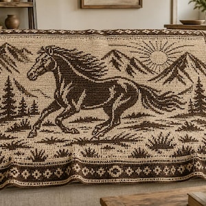 May include: A rectangular crochet blanket featuring a dark brown horse galloping across a landscape with mountains, pine trees, and a sun. The design includes a decorative geometric border in dark brown and cream, with a repeating pattern throughout.