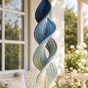 Può includere: Una decorazione a spirale sospesa realizzata in filato lavorato all'uncinetto con una sfumatura di colore verticale che passa dal blu navy scuro in alto al blu chiaro, verde salvia e infine a un bianco crema nella parte inferiore.