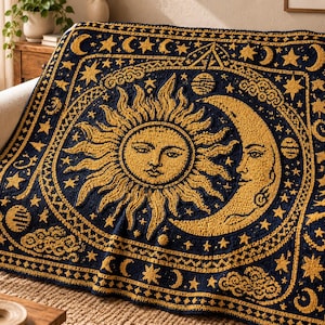 May include: A rectangular throw blanket featuring a dark navy blue background with a prominent golden yellow sun and crescent moon design. The pattern includes celestial motifs such as stars, planets, and clouds, all rendered in a textured knit.