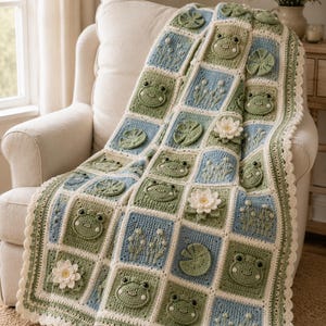 May include: A crochet blanket featuring a grid of squares in shades of sage green, light blue, and cream. The squares display three-dimensional motifs including smiling frogs, white water lilies, green lily pads, and small floral sprigs.