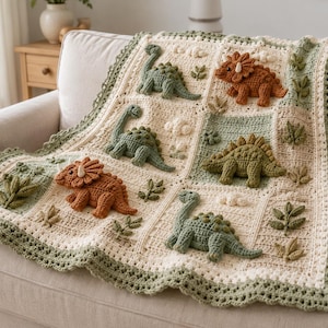 Peut inclure: Une couverture crochetée crème et vert sauge ornée d'applications de dinosaures en relief dans des tons orange rouille et vert sauge. La couverture est décorée de petits motifs de feuilles et de nuages crochetés avec une bordure festonnée.
