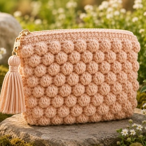Può includere: Una pochette all'uncinetto color pesca caratterizzata da un motivo a punto nocciolina testurizzato sull'esterno. La borsa rettangolare include una chiusura a zip in metallo dorato e una nappa in tessuto abbinata al cursore.