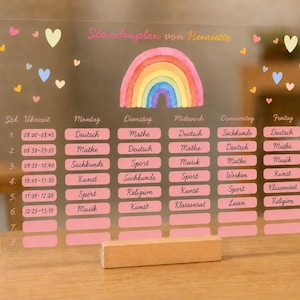 Könnte beinhalten: Ein wöchentlicher Stundenplan aus transparentem Acryl mit Holzsockel. Das Board zeigt einen bunten Aquarell-Regenbogen, kleine Herz-Symbole und den Text "Stundenplan von Henriette". Es enthält Spalten für Wochentage und Zeilen für Zeitintervalle.