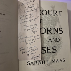 May include: A rectangular white bookmark featuring black cursive text with quotes from the book A Court of Thorns and Roses by Sarah J. Maas. The bookmark displays lines including There you are, I've been looking for you, Hello Feyre darling, and Remember that you are a wolf.