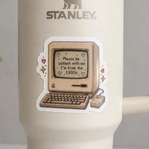 May include: A beige Stanley tumbler featuring a sticker of a vintage beige computer with a keyboard and mouse. The screen displays the text: Please be patient with me I'm from the 1900s, surrounded by small heart and star icons in a light brown color.
