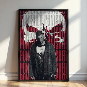 Op de afbeelding: Een ingelijste poster met een centraal portret van een man in een donker jasje met een schedel-embleem op het shirt. De achtergrond toont een grote witte schedelafbeelding met daaroverheen de herhaalde rode tekst PUNISHER.