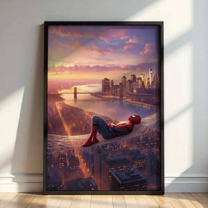 Op de afbeelding: Een ingelijste kunstdruk met een rood en blauw gekleed figuur dat rust op een web boven een stadsskyline bij zonsondergang. De scène bevat een rivier, een brug en verlichte gebouwen onder een levendige oranje en paarse lucht.