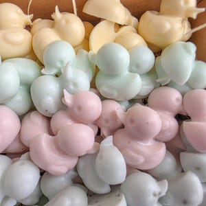 May include: A close-up of a collection of duck-shaped soaps in pastel colours. The soaps are in shades of yellow, green, pink, and white. The soaps are closely packed together. These soaps would be suitable for a baby shower or as a gift.