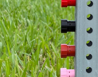 May include: A vertical metal post with a series of circular holes features seven cylindrical knobs in blue, gray, red, black, dark red, pink, and dark green. Each knob has a ridged edge and small perforations along its side, securely attached.