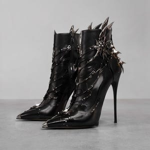 Puede incluir: Un par de botines negros con tacones de aguja altos y puntera afilada. Los botines cuentan con púas de metal plateado en el talón y la punta, con cadenas plateadas decorativas drapeadas en los laterales y un adorno metálico en forma de estrella.