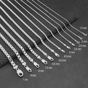 Könnte beinhalten: Eine Sammlung silberfarbener Boxketten, angeordnet nach Breite von 1,5 mm bis 1 cm. Jede Kette hat eine metallische Oberfläche und einen Karabinerverschluss, wobei die spezifische Breite neben jeder einzelnen Kette deutlich beschriftet ist.
