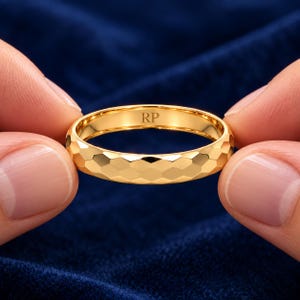 Könnte beinhalten: Ein goldener Ring mit einer facettierten, wabenartigen Außenstruktur. Die Innenseite des Rings ist glatt und deutlich mit den Buchstaben RP graviert. Der Ring hat eine polierte, reflektierende Oberfläche, die das Licht auf seiner Form einfängt.